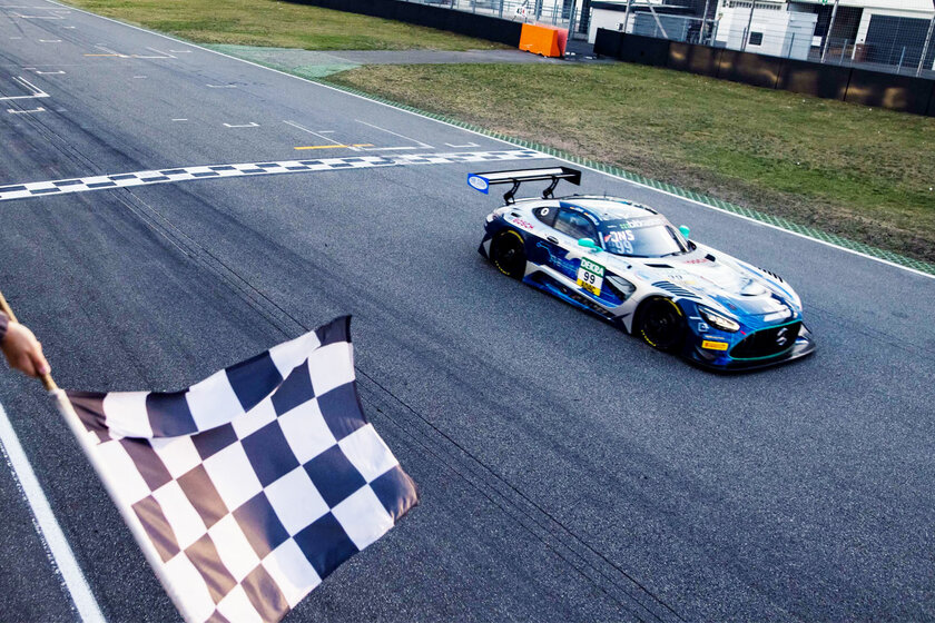 Ein Mercedes GT3 Rennauto von Arnold NextG fährt über die Ziellinie. Links unten schwenkt jemand de Zielflagge.