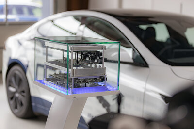 In einem Austellungsstück mit Glaskasten befindet sich ein geöffnetes NX NextMotion Steuergerät, wo man dei Platinen im inneren sehen kann, im Hintergrund befindet sich ein weißer Tesla.
