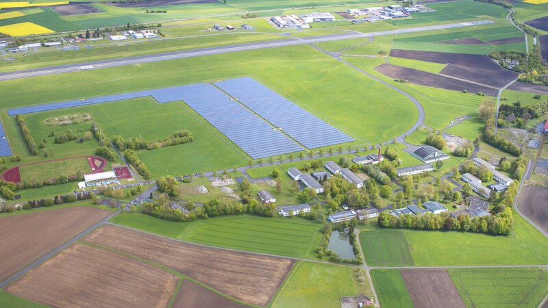 Eine Drohnenaufnahme des New Mobility Campus in Mengen/Hohentengen. Vorne befindet sich der Campus mit Hangar, ein altes Krankenhaus... und im Hintergrund sind Reihen von Solarfeldern zu sein und der Flugplatz von Mengen/Hohentengen.