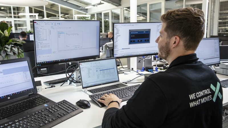 Ein Mitarbeiter der Firma Arnold NextG der im Bereich Softwareentwicklung arbeitet, sitz vor sehr vielen Bildschirmen und arbeitet.
