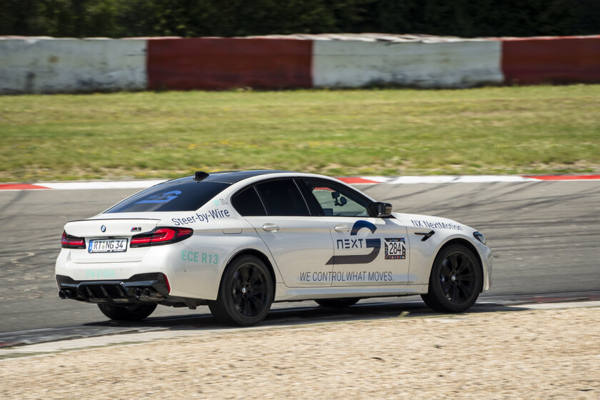 Ein weißer BMW fährt auf einer Rennstrecke ziemlich schnell. Auf dem Auto befinden sich diverse Logos unter anderem das hauptlogo von Arnold NextG.