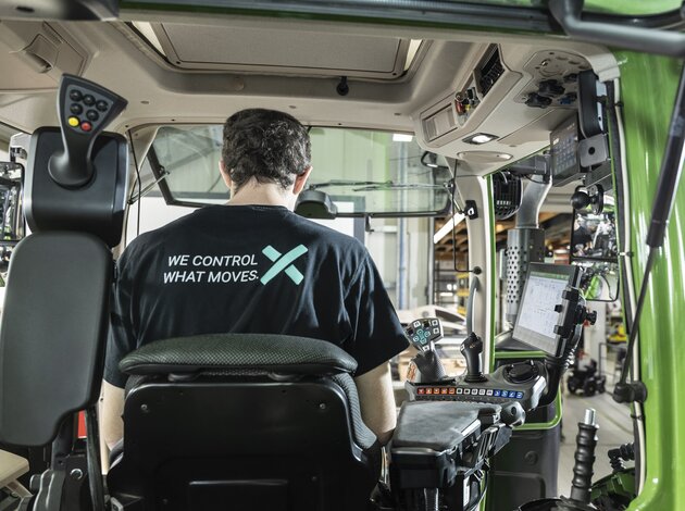 Ein Mitarbeiter der Firma Arnold NextG sieht man von hinten, durch das hintere Fenster einer Traktor Kabine. Auf seinem Tshirt steht groß "We control what moves."