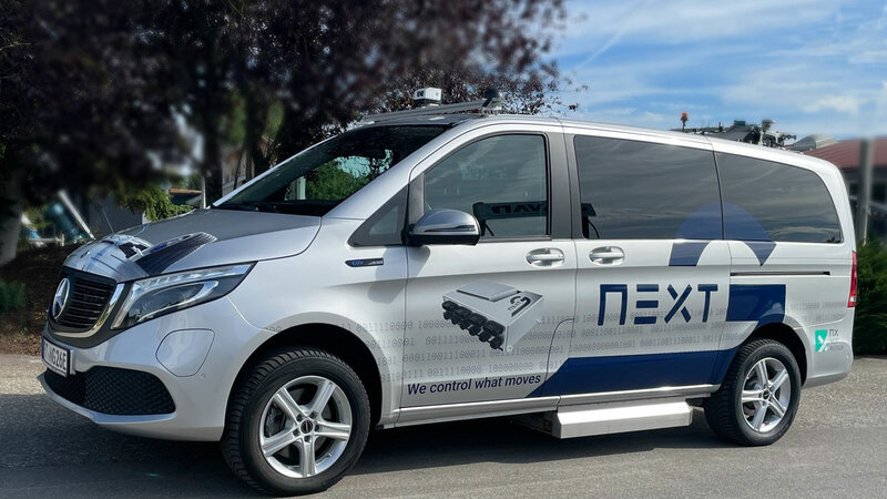 Ein gebrandeter Arnold NextG Mercedes EQV in Silber, steht bei blauem Himmel vor einem Baum.
