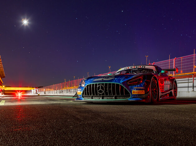 Bei klarem Sternenhimmel und Mondschein, steht das Rennauto von Arnold NextG, ein Mercedes GT3, in der beleuchteten Boxengase von Oschersleben. Das Rennauto steht rechts mit der Schnauze nach vorne, was mit dem roten Licht der Boxengasse sehr gefährlich wirkt.