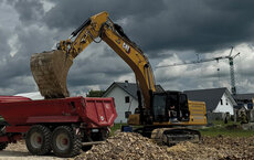 Ein 36-Tonnen-Raupenbagger von Caterpillar lädt Aushubmaterial in einen roten Muldenkipper auf einer Baustelle.