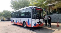 Ein weiß roter Bus steht am Straßenrand bei strahlendem Sonnenschein. Ein paar Menschen stehen auf dem Bürgersteig neben dem Bus.