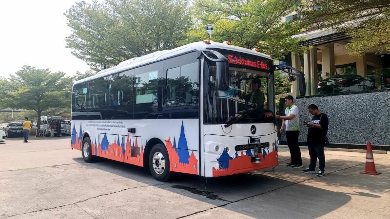 Ein weiß roter Bus steht am Straßenrand bei strahlendem Sonnenschein. Ein paar Menschen stehen auf dem Bürgersteig neben dem Bus.