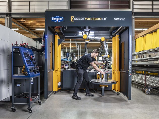 Ein Mitarbeiter der Fertigung von Arnold NextG steht in einem Cobot WeldSpace 4.0, einem Schweißroboter und stellt den Roboterarm in die richtige Position.