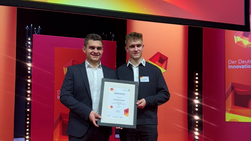 Kevin und Luca Arnold strahlen bei einer Preisverleihung. Alles um die beiden leuchtet rot. Kevin und Luca Arnold halten in ihrer Mitte eine Urkunde fest.