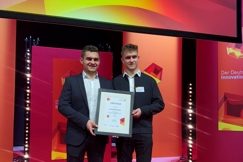 Kevin und Luca Arnold strahlen bei einer Preisverleihung. Alles um die beiden leuchtet rot. Kevin und Luca Arnold halten in ihrer Mitte eine Urkunde fest.