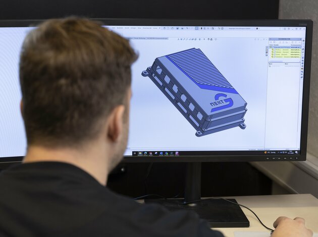 Ein Kopf eines Mannes schaut auf den vor ihn offenen Bildschirm. Auf dem Bildschirm ist eine CAD Zeichnung des NX NextMotion zu sehen.