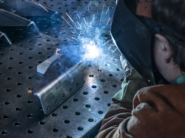 Ein Mitarbeiter der Fertigung von Arnold NextG schweißt zwei Metallstücke zusammen, was ein blaues starkes Licht erzeugt.