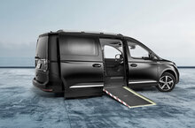Ein tiefergelegter schwarzer VW Caddy, umgebaut mit NX NextMotion für Selbstfahrer, steht auf einem großen Platz mit geöffneter Seiteneinstiegsrampe – ohne Fahrersitz.