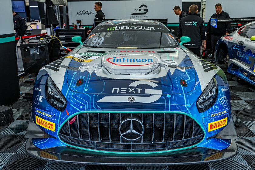 Ein Mercedes GT3 von Arnold NextG frontal fotografiert in seiner Box. Im Hintergrund stehen mehrere Mechaniker.