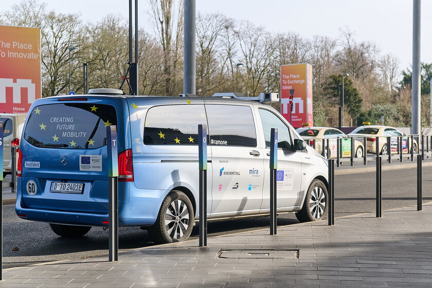 Ein Blau, Silbernes Fahrzeug steht an der Seite einer Straße neben Pollern. Auf dem Auto befindet sich ein Kamerasystem für das Autonome/teleoperierte Fahren.