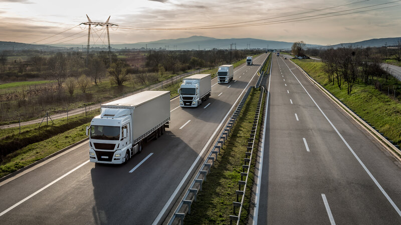 Mehrere Lkw fahren im perfekten Abstand zueinander als Platooning Lösung auf der rechten Spur einer Autobahn.