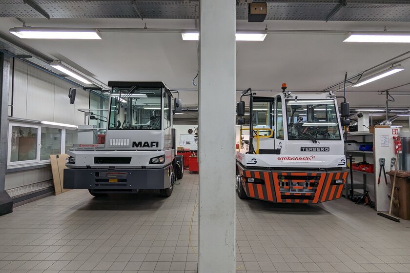 In der Werkstatt von Arnold NextG stehen zwei Terminal Trucks nebeneinander. Der Linke ist grau weiß und von der Firma MAFI Transport System GmbH und der rechte ist rot grau weiß von der Firma Terberg.