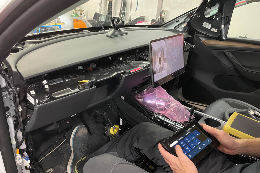 Ein Innenraum eines Autos, welches sich im Umbau befindet. Es existiert kein Lenkrad mehr und ein Mensch sitzt auf dem Fahrersitz und hält ein Touch Display für diverse Funktionen am Auto.