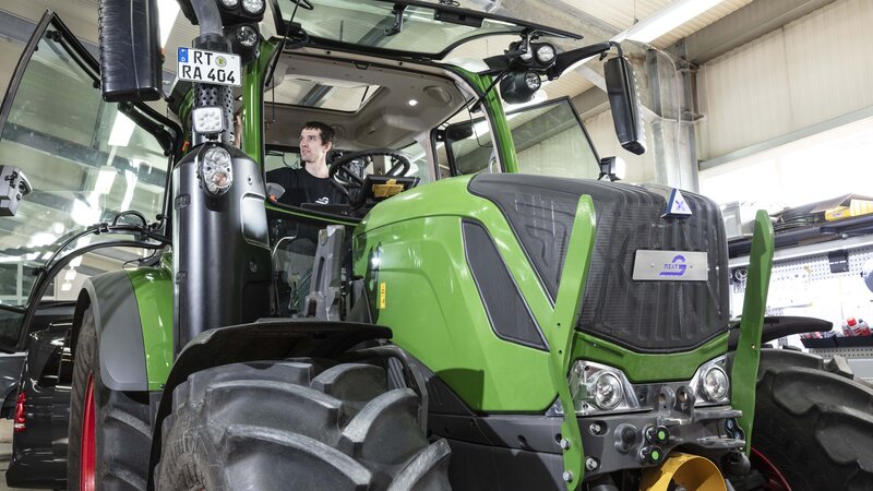 Ein hellgrüner Traktor, umgerüstet mit NX NextMotion, wird von einem Techniker in der Werkstatt getestet, während er in der Kabine sitzt.
