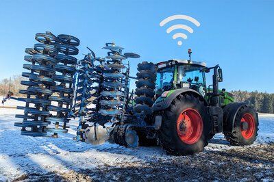Ein Traktor mit zusammengeklappten Anbaugerät steht auf einem Schneebedecktem Feld.