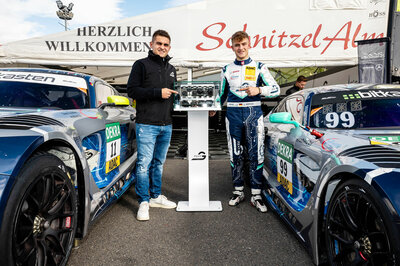 Kevin und Luca Arnold stehen rechts und links von unserem Austellungsstück, das NX NextMotion. Luca Arnold steht im Rennanzug da, Kevin Arnold in Jeanshose und schwarzer Jacke. Neben den beiden steht jweils noch ein Mercedes GT3 Rennauto. Dahinter befindet sich noch ein großen weißes Zelt von SchnitzelAlm Racing.  