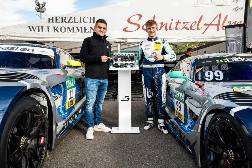 Kevin und Luca Arnold stehen rechts und links von unserem Austellungsstück, das NX NextMotion. Luca Arnold steht im Rennanzug da, Kevin Arnold in Jeanshose und schwarzer Jacke. Neben den beiden steht jweils noch ein Mercedes GT3 Rennauto. Dahinter befindet sich noch ein großen weißes Zelt von SchnitzelAlm Racing.  