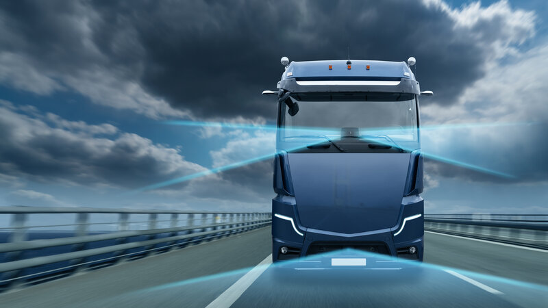 Ein animiertes Bild eines blauen LKW der frontal auf einer Straße fährt bei dunklen Gewitterwolken am Himmel. Vom LKW gehen blaue digitale Sensorstreifen nach vorne weg und auf.