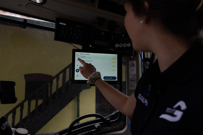 Eine Dame sitzt in einer Kabine und drückt auf ein Touch Display mit einem Finger.