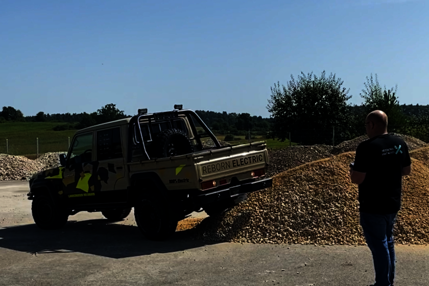 Ein Toyota Landcruiser mit Doppelkabine für Untertagebau/Bergbau in braun mit schwarz und neonfarbenen Highlights, fährt mit dem rechten Hinterrad auf einen Schotterhaufen, gesteuert von einem Arnold NextG Mitarbeiter der zum Toyota schaut und eine Fernsteuerung in der Hand hat.