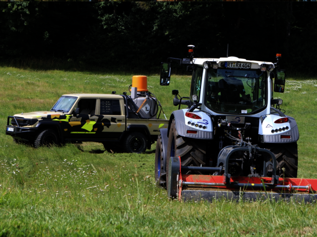 Autonom fahrender Traktor mit Anbaugerät und umgebauter Geländewagen mit Sensorik-System auf einer grünen Wiese bei Testfahrt.