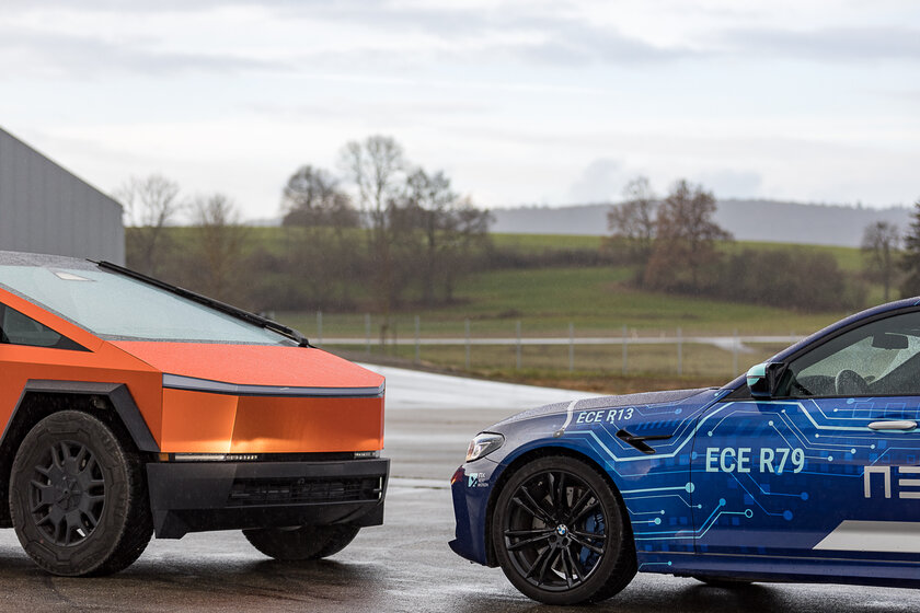 Zwei Autos stehen Schnauze an schnauze gegenüber. Das hintere ist ein orangener Cybertruck, das vordere ein blau gebrandeter BMW von Arnold NextG.